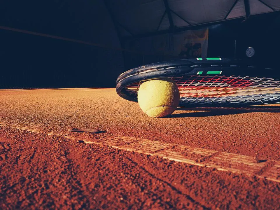 Raqueta de tenis y pelota apoyadas sobre una pista de tierra batida
